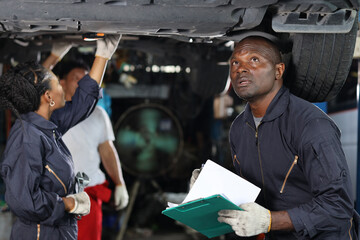 Obraz premium Group of car mechanic in uniform checking maintenance a lifted car service with clipboard at repair garage station. Worker holding wrench and fixing breakdown vehicle. Car repair service concept