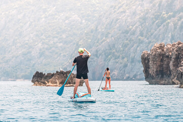 Naklejka premium Group or team with paddles swims on a SUP boards on the sea near scenic rocks. Healthy lifestyle and recreation concept