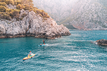 Aerial view of a group or team with paddles swims on a SUP boards on the sea near scenic rocks....