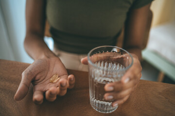 African American girl holds pill or tablet in hand and glass of water close up. Medication drugs, vitamin or dietary supplement.