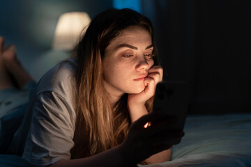 Addicted young woman chatting and surfing on the Internet with smartphone late at night in bed....