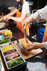 Close-up of female worker of street food truck putting minced meat into bun while preparing...