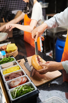 Close-up of female worker of street food truck putting minced meat into bun while preparing appetizing hotdog for hungry consumer