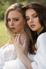 Two beautiful caucasian girls in wedding dresses look at the camera