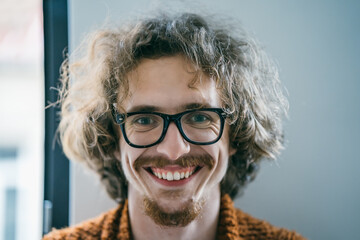Portrait of positive smiling young man in glasses looks at camera.