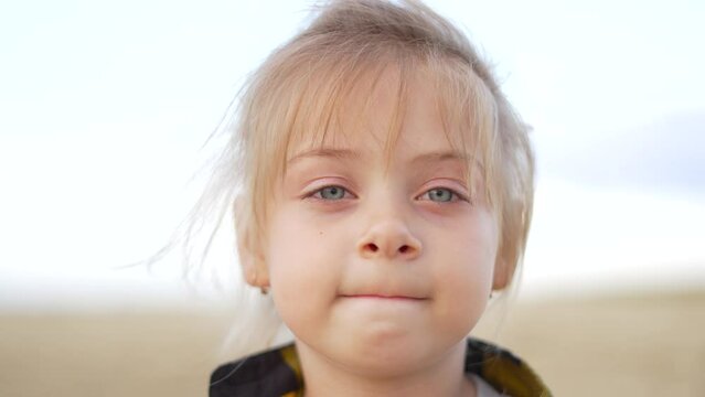 Close-up portrait of cute fair-haired girl. child looks into camera lens. One baby girl with blond hair looks forward into camera. Cute little girl face closeup