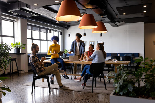 Happy diverse male and female colleagues using laptop talking in casual office meeting