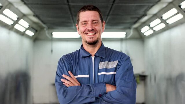 Professional car repair shop owner standing in front of repainting room with auto parts, happy mechanic or technician cross arms smiling action, Caucasian small business owner lifestyle concept
