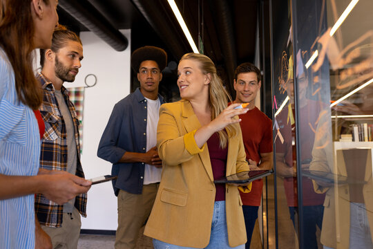 Happy diverse creative colleagues in discussion brainstorming making notes on glass wall in office