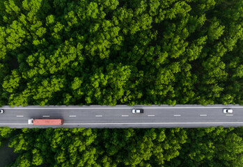 Aerial top view of car and truck driving on highway road in green forest. Sustainable transport....