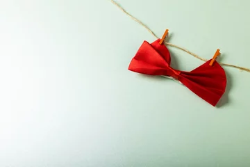 Poster High angle view of red bowtie hanging with clothespins on clothesline against white background © vectorfusionart