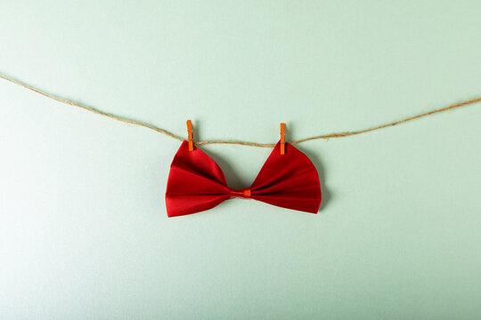 Close-up of red bowtie hanging with clothespins on clothesline against white background, copy space