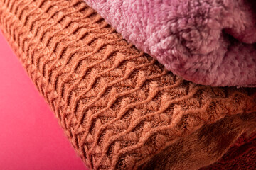 Close-up of brown and pink sweaters stacked and arranged on pink background, copy space
