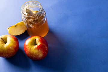 High angle view of honey with dipper in jar with apples against blue background, copy space
