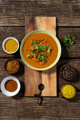 Directly above shot of meat gravy with spices and lentils in bowls and cilantro on wooden table