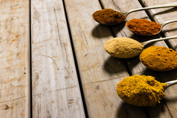 High angle view of various ground spices in spoons arranged on wooden table