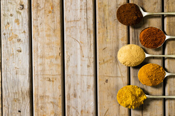 Directly above shot of various ground spices in spoons arranged on wooden table