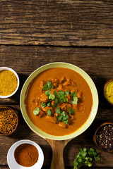 Overhead view of meat gravy in bowl with spices, cilantro and lentils over wooden table