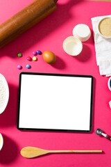 Overhead view of digital tablet with egg, candies, cupcake holders and rolling pin, copy space
