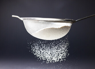 Close-up of flour sifting by sieve against black background, copy space