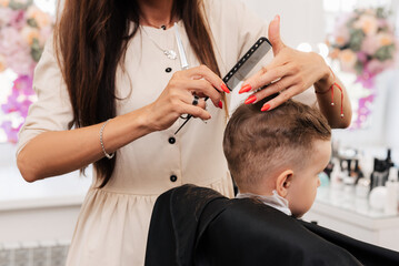 Shooting in a beauty salon. A hairdresser gives a haircut to a little boy with scissors.