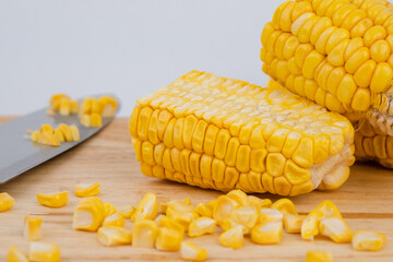 Sweet corn kernels are cut from the cob on a wooden cutting board with a knife. Using corn kernels in cooking to make delicious desserts.