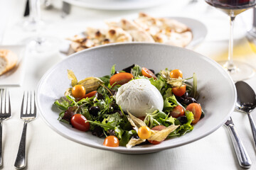 Buffalo salad with greens, tomatoes, physalis, olives and the mozzarella as a centerpiece