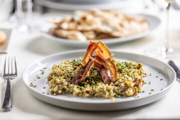 Decorative crunchy bacon on top of pistchio risotto in a shallow plate