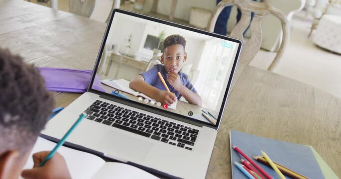 African american boy using laptop for video call with african american school friend on screen