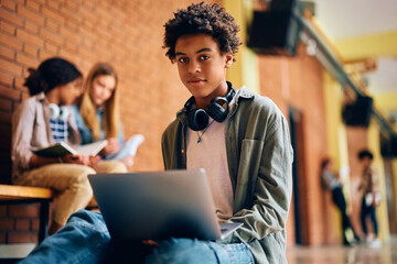 Black high school student using laptop and looking at camera.