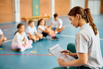 Fototapeta na wymiar Female sports teacher going through exercise plan during PE class at school gym.