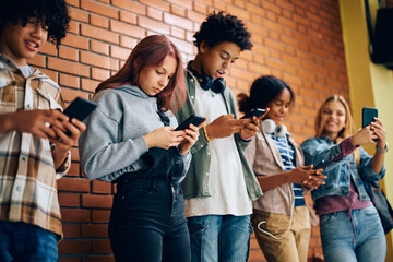 Multiracial group of teenagers using their cell phones at high school.