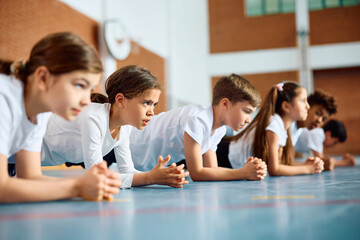 Group of schoolkids exercising during PE class at school gym.