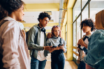 Multiracial group of teenage friends talk in hallway at high school.