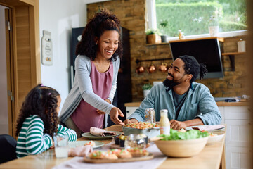 Happy black mother serving food to her family at dining table.