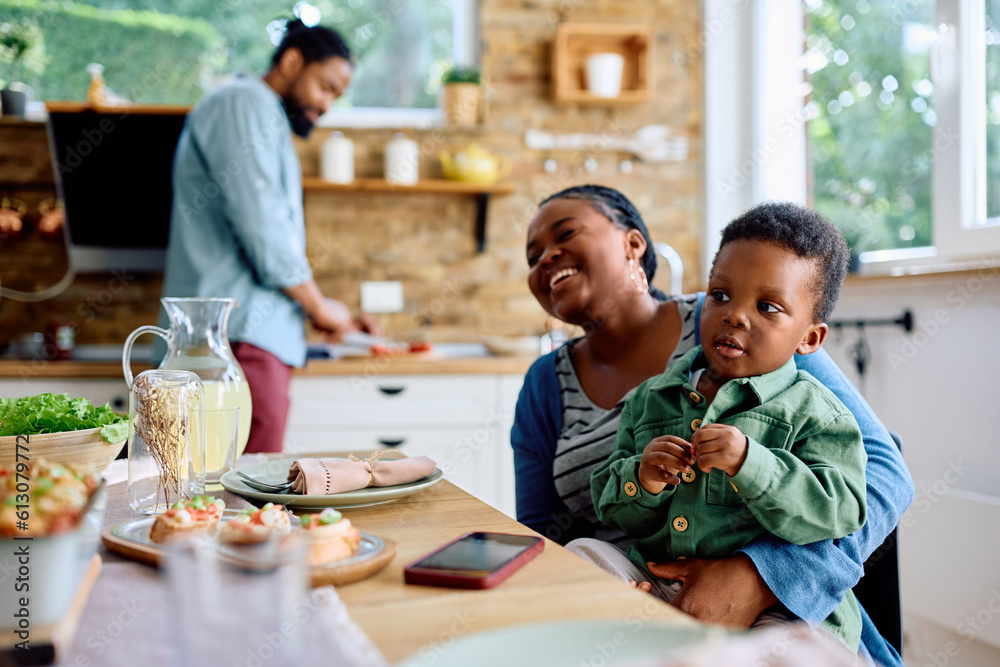 Wall mural Little black boy sitting on mother's lap at dining table.