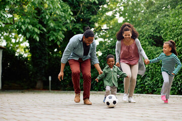 Happy black parents and their kids playing with soccer ball in park. © Drazen