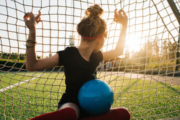 girl sat in a football goal looking away into the distance