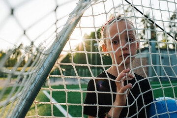 Girl stood goal holding a football looking through the goal net