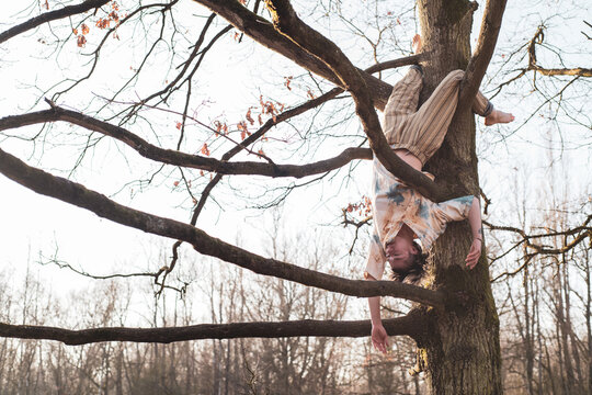 asian dancer hangs upside down from tree branches in nature