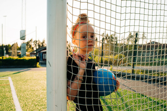 portrait of a girl holding a football stood by a goal
