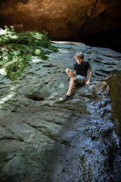 Child on summer hike playing on rocky waterfall