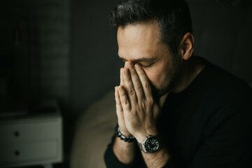 Sad man put his hands to his face sitting on the bed