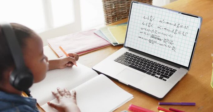 African american girl taking notes and using laptop with mathematical equations on screen