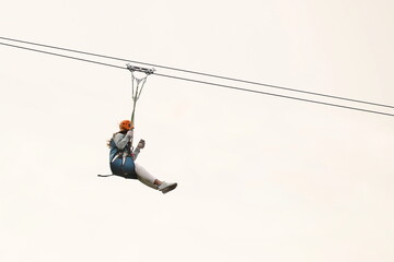 A woman in a rock climbing outfit slides down a steel cable on a roller gurney against the sky. Extreme recreation and sports. Amusement park for brave people. Outdoor activity. dangerous hobby