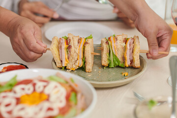 Hands of young man holding wooden toothpicks with appetizing homemade canapes on plate prepared for guests of home party