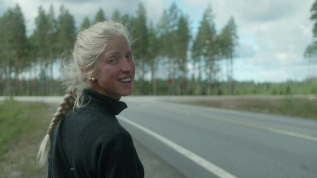 Beautiful Blonde Girl Hitch Hiking on a Cross Road, Finland Countryside, Female Autostopper with Heavy Backpack in Scandinavia, The Cars are not Stopping, Close-up from Behind