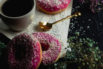Close-up on a pink glaze with a white sprinkle. Doughnuts on the table with coffee.