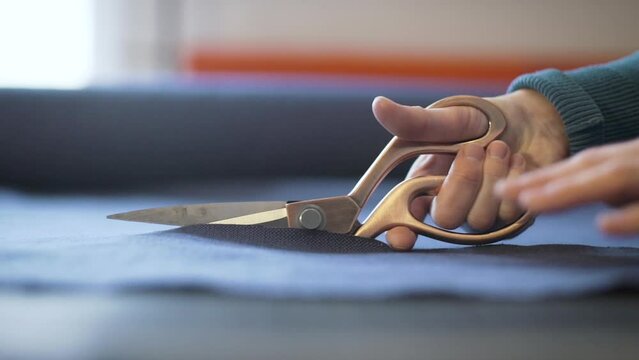 Hand holding big scissors and making cut of tissue. Probably it is tailor, designer, stylist or dressmaker making clothes in his or her studio. Close up shot.