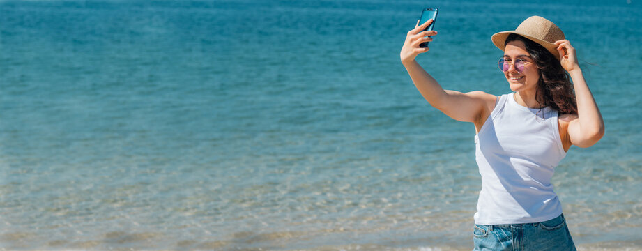 happy girl taking a selfie or live video on the beach with copy space